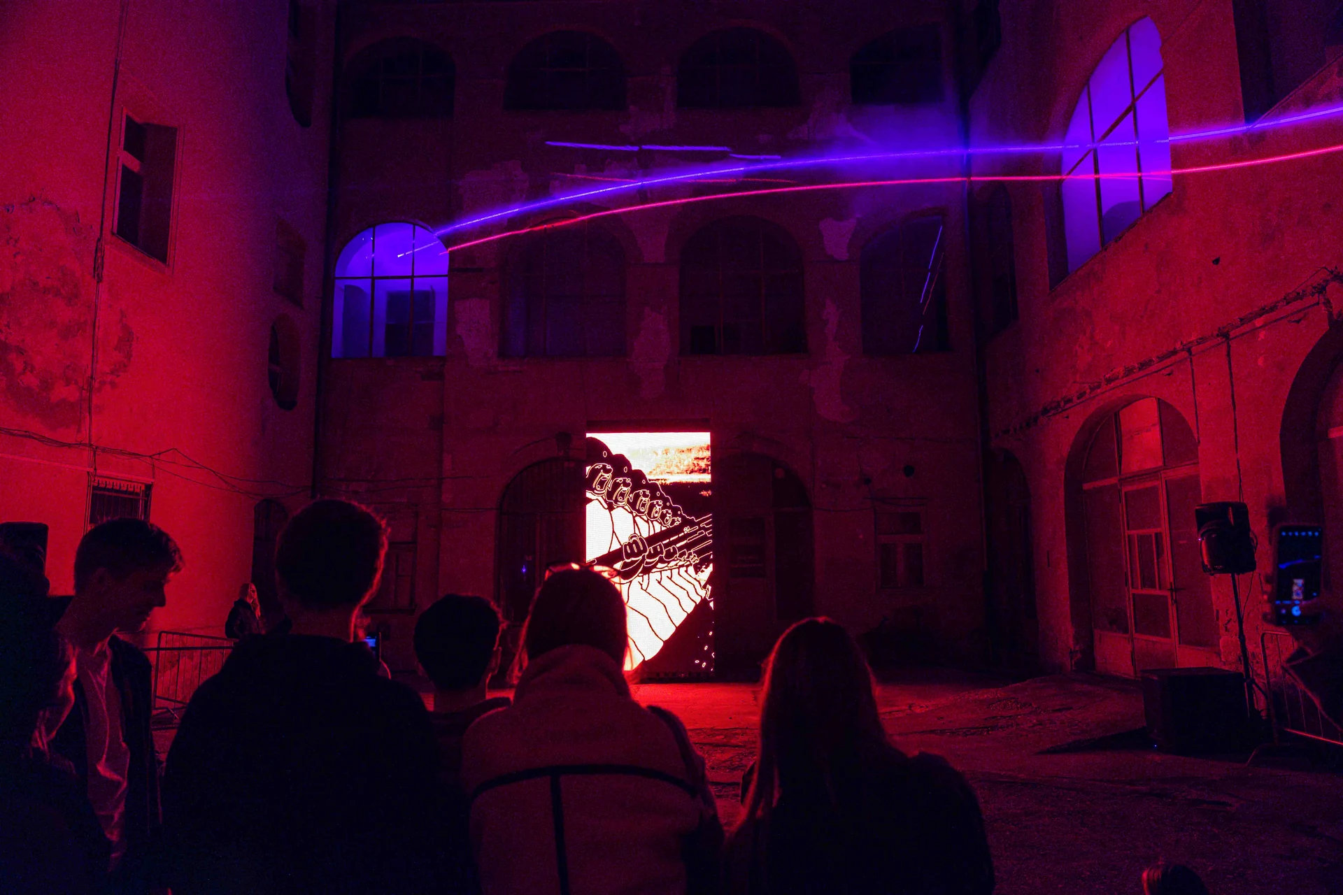Visitors watching a red and violet projection in an outdoor courtyard