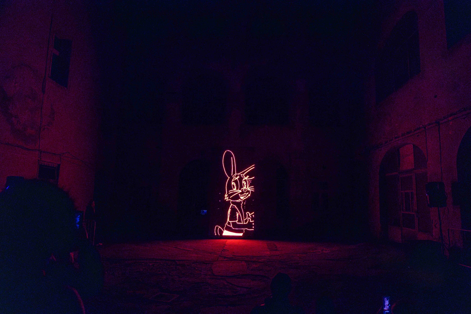 A projected figure glowing in a dark courtyard